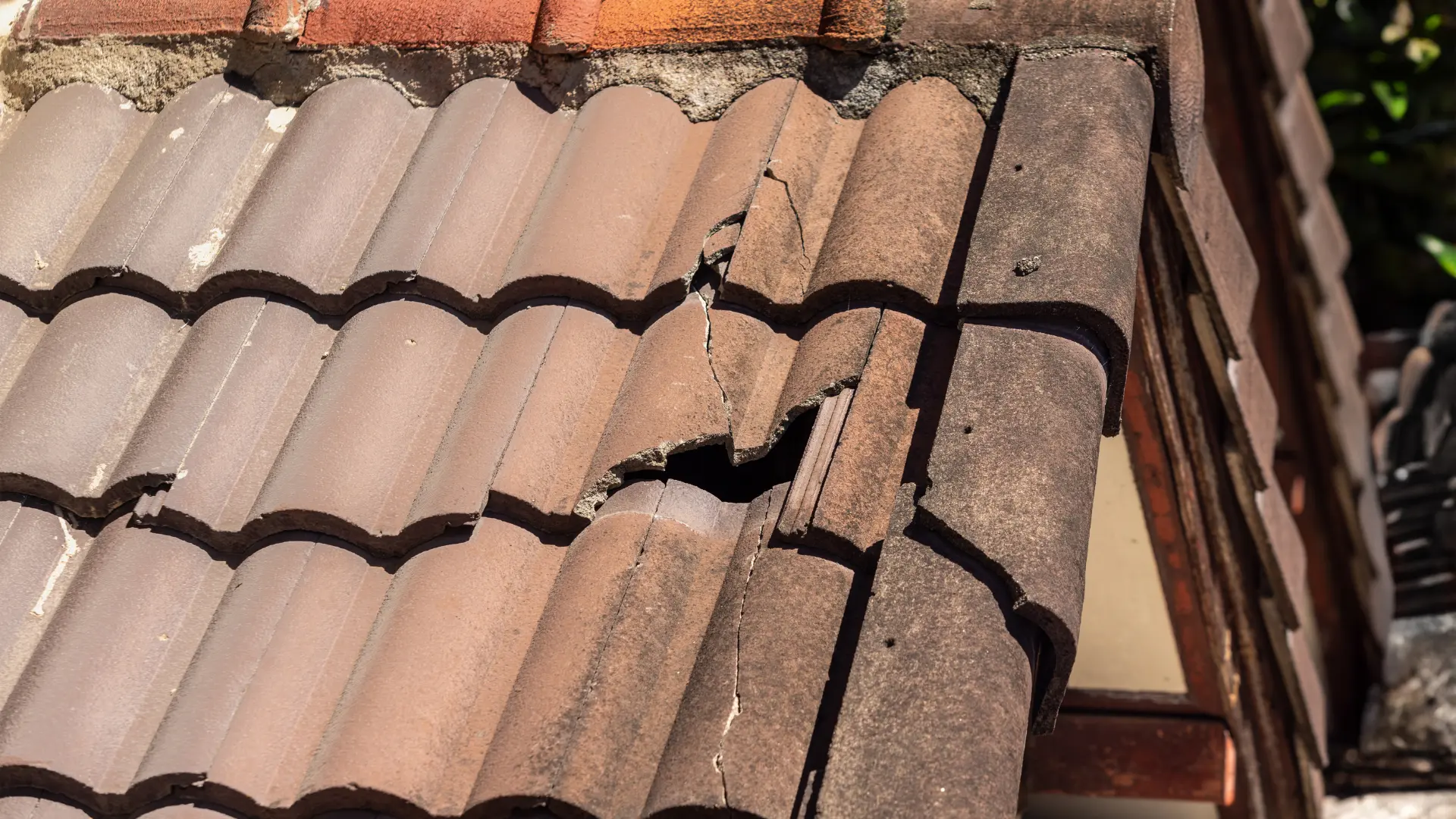 Cracked and holed roof tiles at a verge after storm damage, needing emergency roof repair