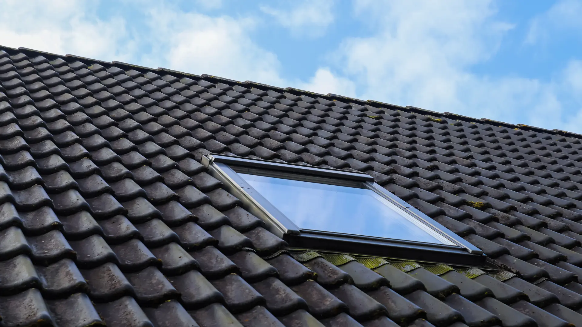 Velux roof window installed flush into a dark tiled pitched roof with a weathertight flashing kit