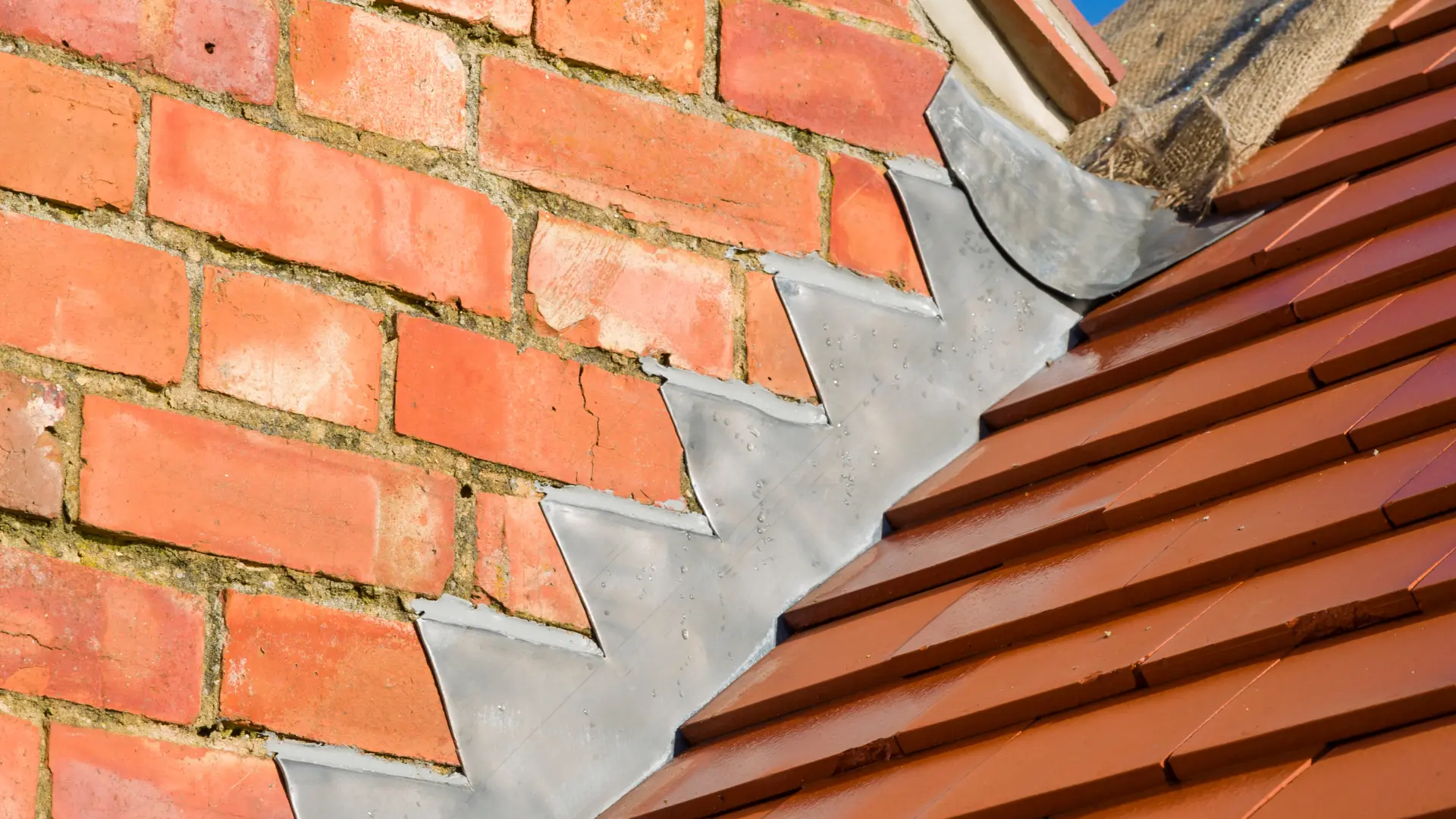 Hand-dressed stepped lead flashing chased into red brickwork above a clay tiled roof