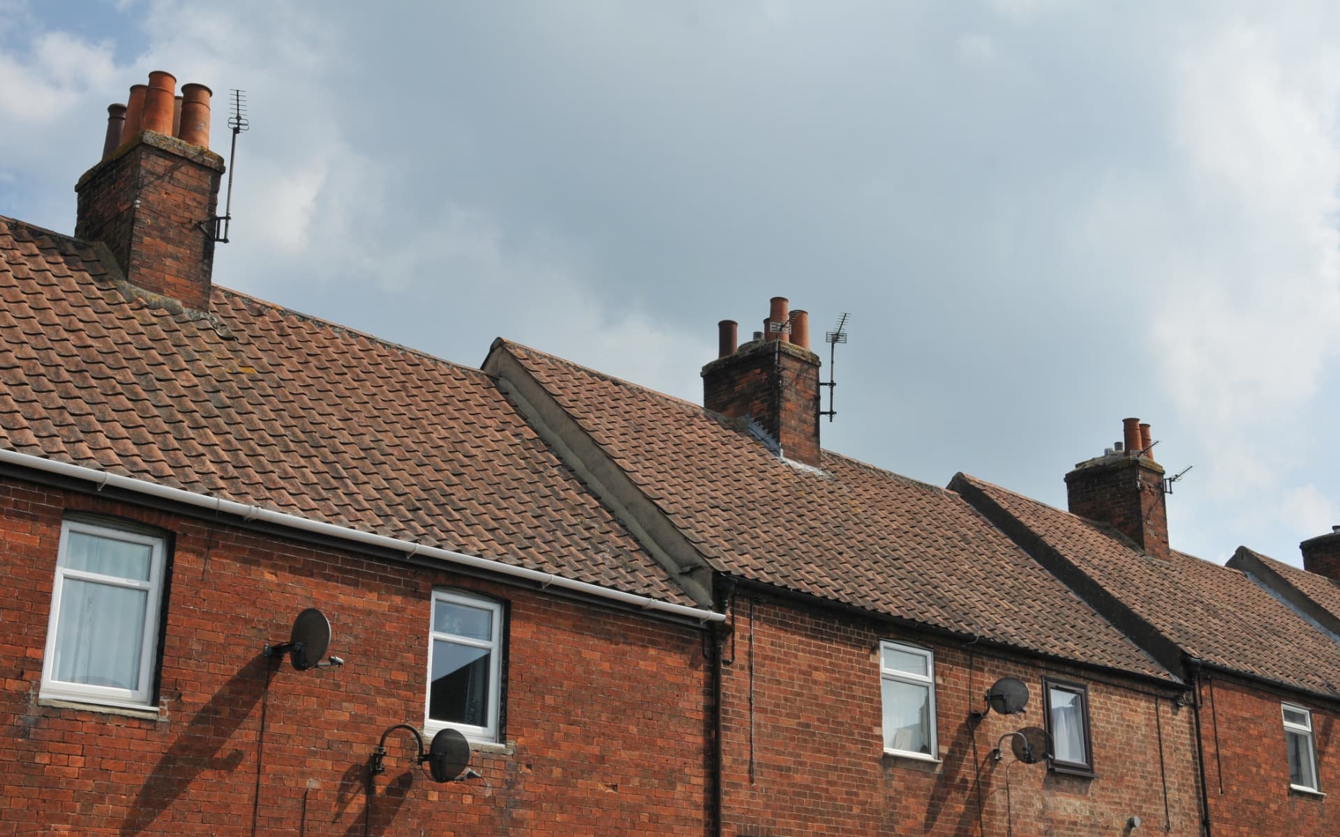 Row of brick terraced cottages with tall clay chimney pots and lead-flashed brick chimney stacks on a clay tiled roof